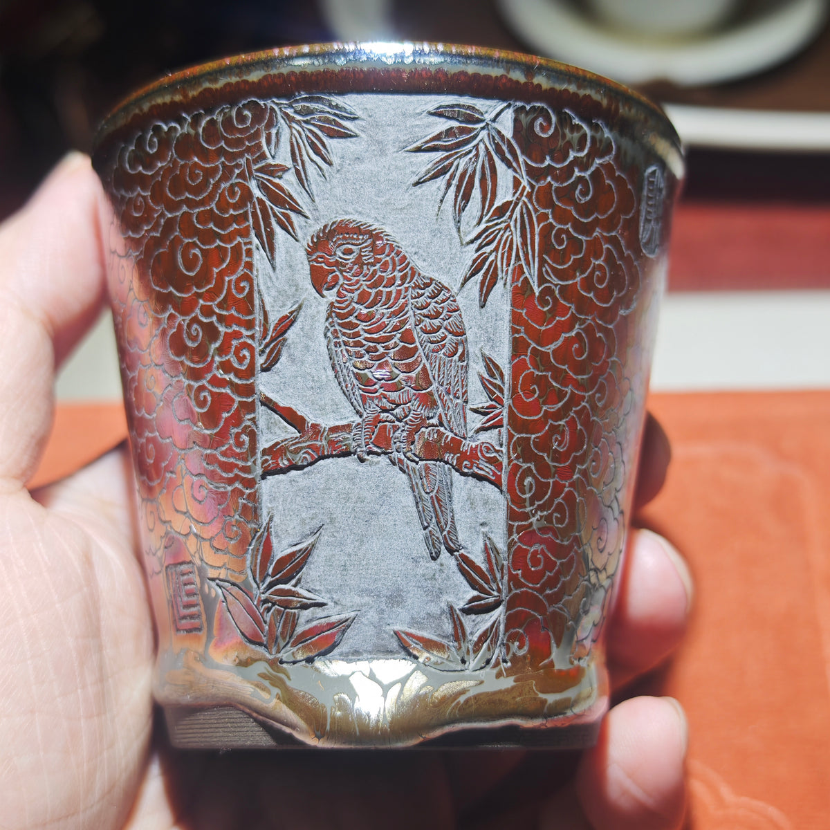 The parrot perches on a branch, with an orange-red glazed Jian tea cup, hand-carved