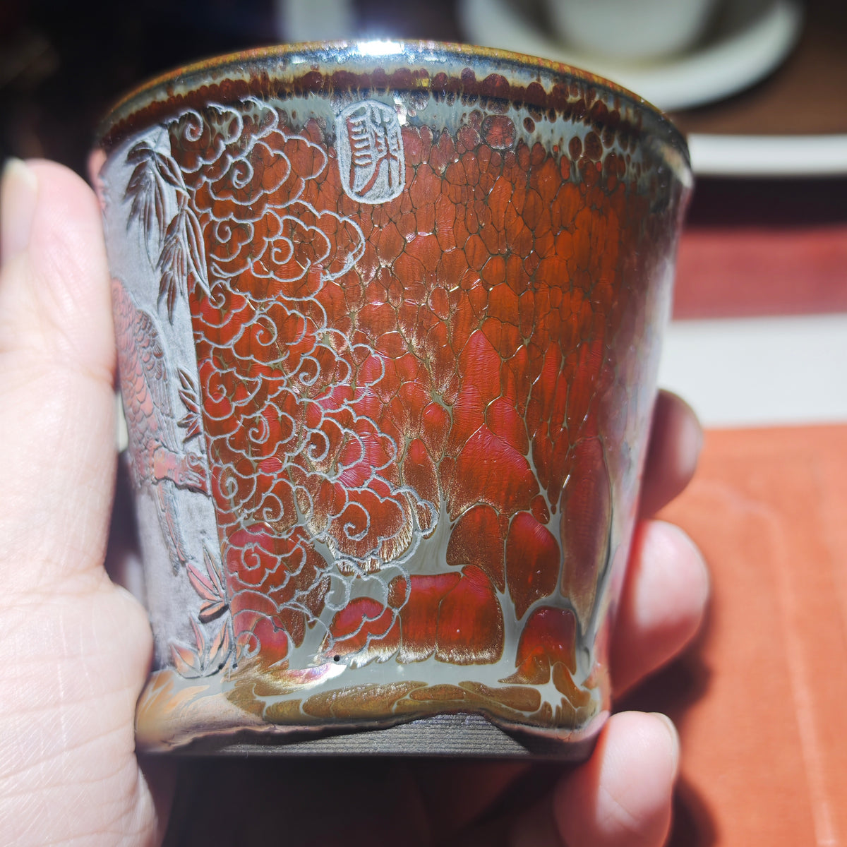 The parrot perches on a branch, with an orange-red glazed Jian tea cup, hand-carved