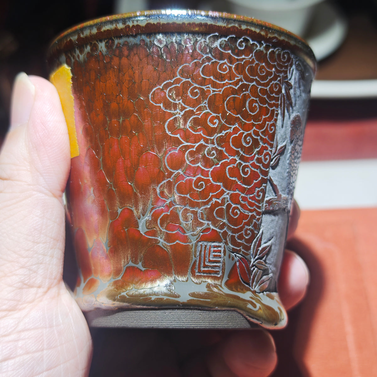 The parrot perches on a branch, with an orange-red glazed Jian tea cup, hand-carved